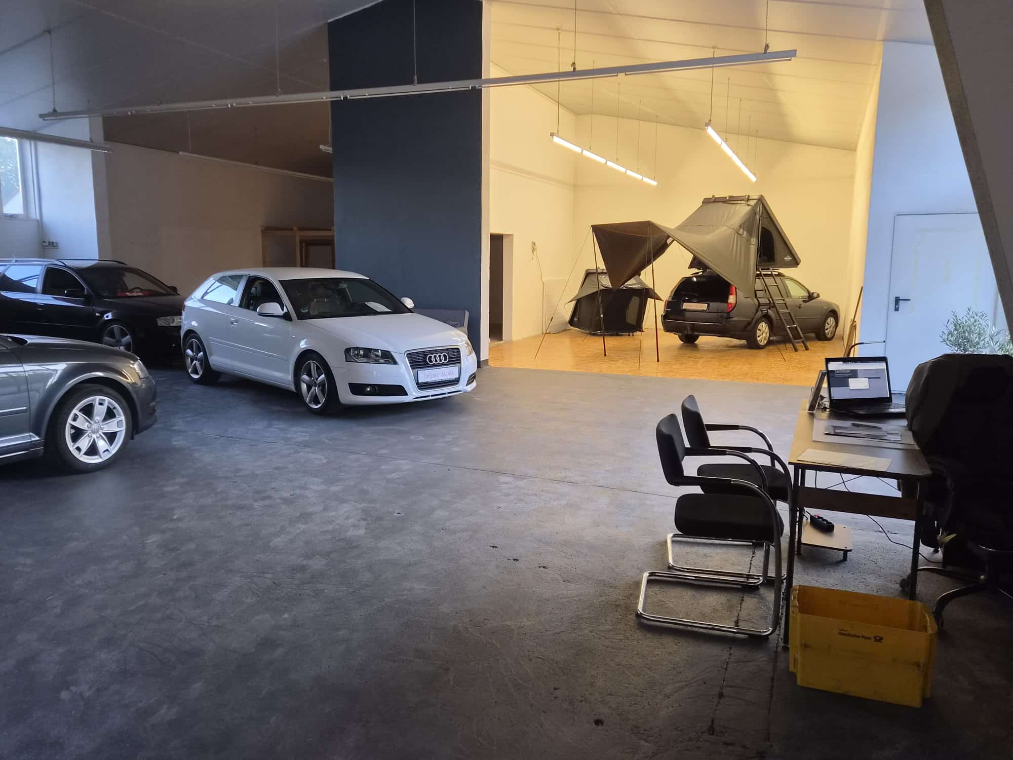 Die Halle von CarSpoint Bavaria: vorne stehen Gebrauchtwagen zum Verkauf, im hinteren, hell beleuchteten Teil zwei aufgebaute Dachzelte.