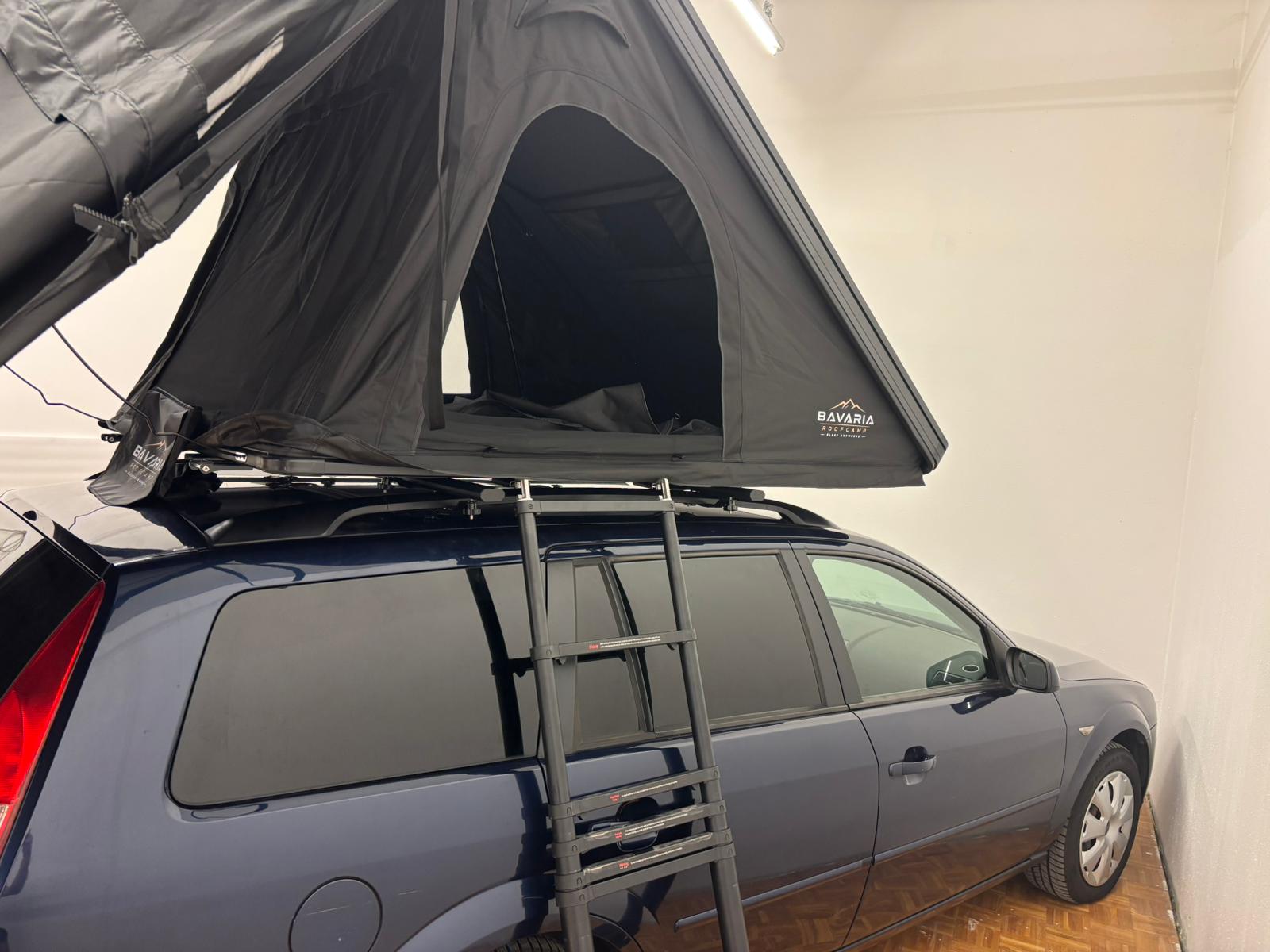 Ein geöffnetes Dachzelt auf dem Dachträger eines dunkelblauen Ford Mondeo Kombi, die Teleskopleiter führt zum Eingang hinauf.