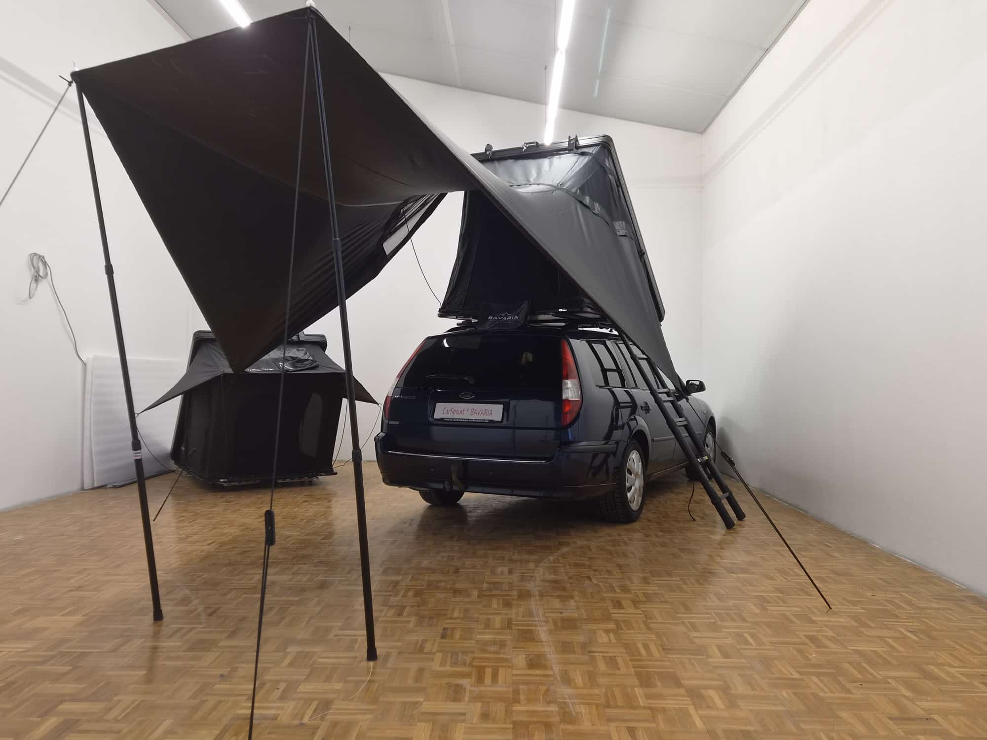 Blick von hinten auf den Kombi: Dachzelt geöffnet, Leiter angelegt, das Sonnensegel überdacht die Fläche neben dem Auto.