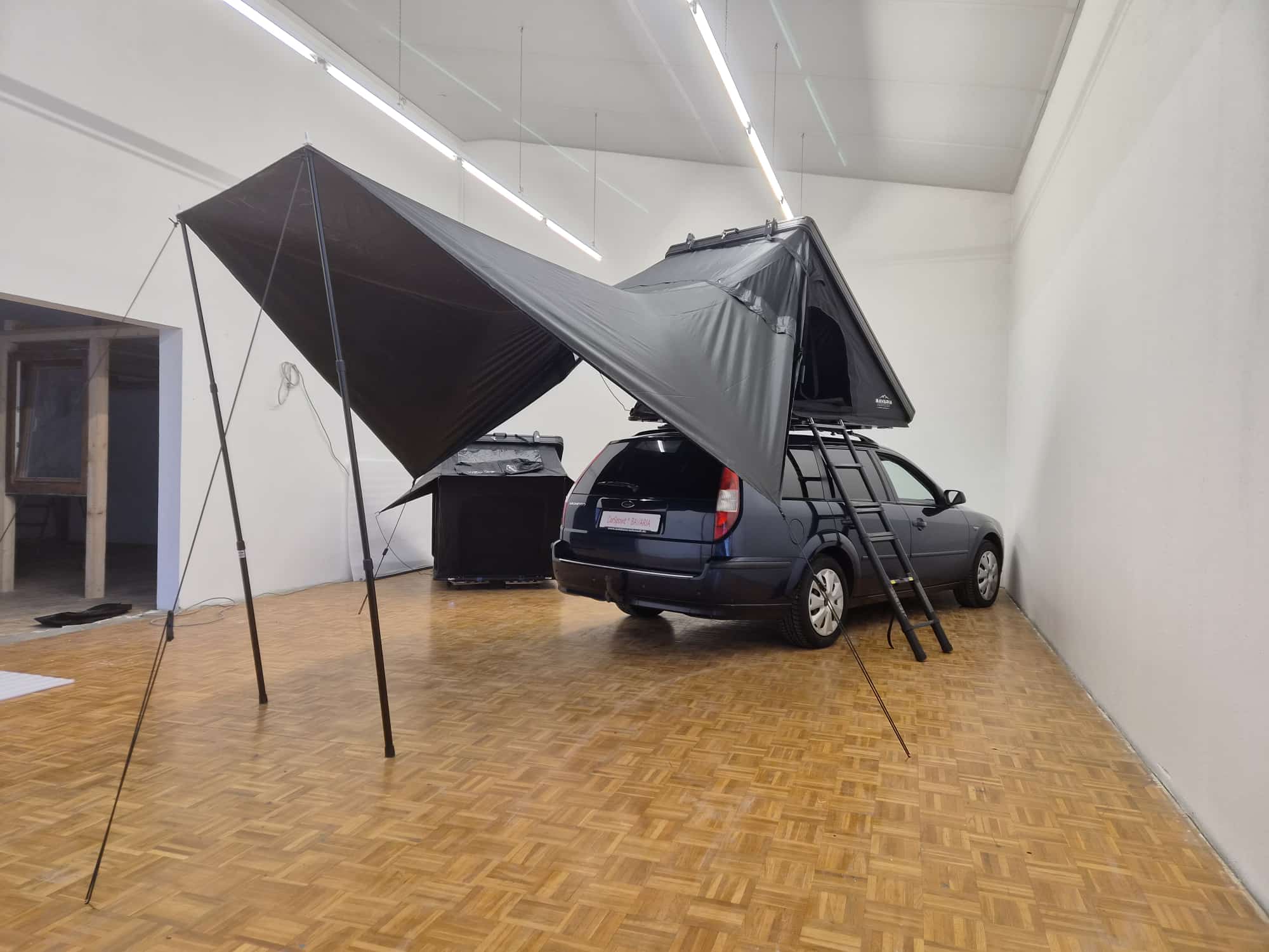 Das Sonnensegel in voller Spannweite seitlich am Fahrzeug, abgespannt mit zwei Teleskopstangen und Leinen.