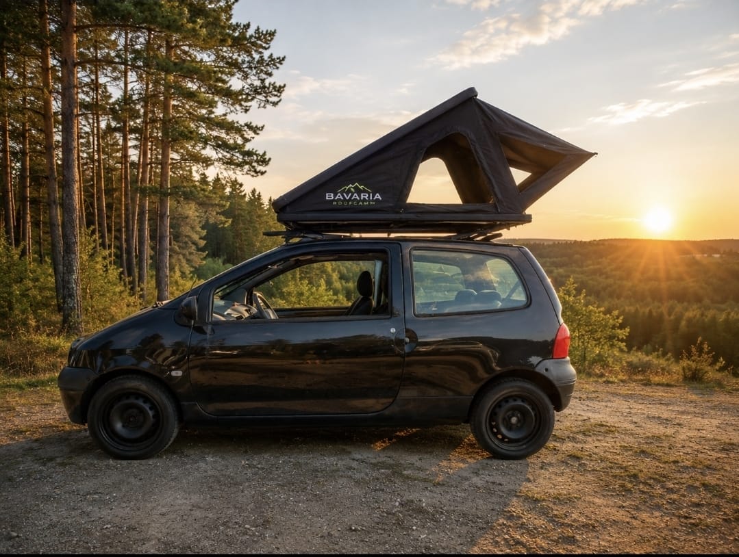 Ein schwarzer Renault Twingo mit geöffnetem Dachzelt steht bei Sonnenuntergang an einem Waldrand.